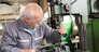 elderly worker watches processing of detail on milling machine