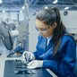 Young Female Blue and White Work Coat is Using Plier to Assemble Printed Circuit Board for Smartphone. Electronics Factory Workers in a High Tech Factory Facility.