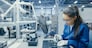 Young Female Blue and White Work Coat is Using Plier to Assemble Printed Circuit Board for Smartphone. Electronics Factory Workers in a High Tech Factory Facility.
