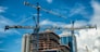 Cranes on modern skyscraper construction in city at sunny day with blue sky