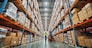 Warehouse worker walking with a forklift in a large warehouse full of shelves