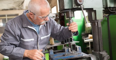 elderly worker watches processing of detail on milling machine
