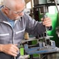 elderly worker watches processing of detail on milling machine