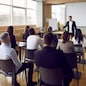 Team of people having class with business trainer. Group of male and female employees sitting at desks in modern office and listening to lecture by experienced teacher sharing knowledge and guidance