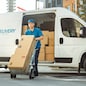 Delivery Man Pushes Hand Truck Trolley Full of Cardboard Boxes Hands Package to a Customer. Courier Delivers Parcel to Man in Business District.