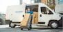 Delivery Man Pushes Hand Truck Trolley Full of Cardboard Boxes Hands Package to a Customer. Courier Delivers Parcel to Man in Business District.