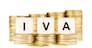 Taxation concept. The letters IVA (Spanish Value Added Tax) on dice on piles of gold coins on a white background.