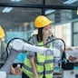 Trainees analyze technical blueprint, program, control robotic arm during practical learning lesson in robot system programming at a manufacturing academy. Emphasizing hands-on experience and skills.