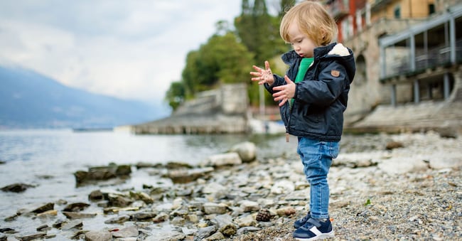 Cute toddler boy playing with pebbles in the harbor of Varenna, one of the most picturesque towns on the shore of Lake Como. Varenna, Lombardy, Italy.