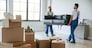 Holding heavy sofa. Two moving service employees in a room.