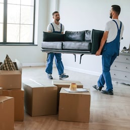 Holding heavy sofa. Two moving service employees in a room.