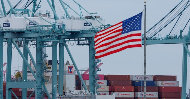 Una bandiera statunitense sventola vicino a dei container mentre una nave viene scaricata al porto di Los Angeles, a San Pedro, California, Stati Uniti, 1 maggio 2025. Foto REUTERS/Mike Blake/File