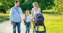 active big family father, mother, son and baby in stroller walking in the park