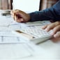 Close-up shot. business owner holding pencil checking report documents and use calculator to manage financial documents bills invoices pay utilities calculate business commercial cost income and tax