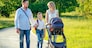 active big family father, mother, son and baby in stroller walking in the park