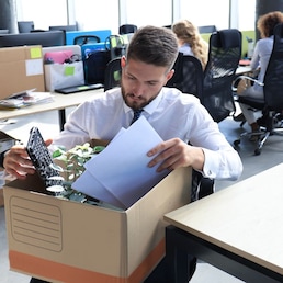 Sad dismissed worker are taking his office supplies with him from office.