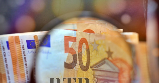 Magnifying glass over the pile of money with the text “BTP” translating as Italian government bonds.