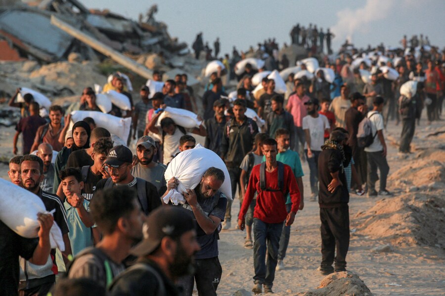 Persone con sacchi di farina camminano lungo via al-Rashid, nella parte occidentale di Jabalia, dopo che camion di aiuti umanitari sarebbero entrati nella Striscia di Gaza settentrionale attraverso il valico di confine di Zikim, controllato da Israele, nel mezzo della guerra in corso tra Israele e Hamas. (Foto di BASHAR TALEB / AFP) (AFP)
