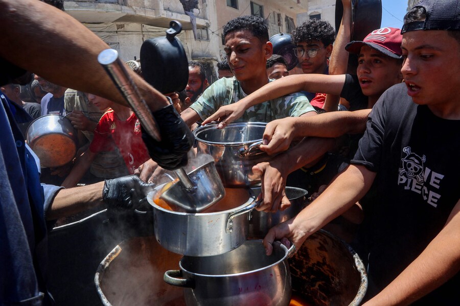 Palestinesi cercano di procurarsi cibo in una mensa di beneficenza che fornisce pasti caldi nel quartiere di Rimal a Gaza City, il 18 giugno 2025, nel mezzo della guerra in corso tra Israele e il movimento palestinese Hamas. La situazione umanitaria a Gaza rimane disastrosa nonostante gli aiuti stiano iniziando a tornare nel territorio dopo oltre due mesi di blocco israeliano. Gli esperti di sicurezza alimentare affermano che la fame incombe su una persona su cinque. Israele ha anche intensificato la sua offensiva militare in quello che definisce un rinnovato tentativo di distruggere Hamas, il cui attacco del 7 ottobre 2023 ha innescato la guerra. (Foto di Omar AL-QATTAA / AFP) (AFP)