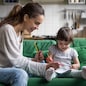 Smiling baby sitter and preschool kid girl drawing with colored pencils sitting on sofa together, single mother and child daughter playing having fun, creative family activities at home concept