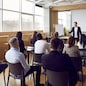 Team of people having class with business trainer. Group of male and female employees sitting at desks in modern office and listening to lecture by experienced teacher sharing knowledge and guidance