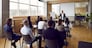 Team of people having class with business trainer. Group of male and female employees sitting at desks in modern office and listening to lecture by experienced teacher sharing knowledge and guidance