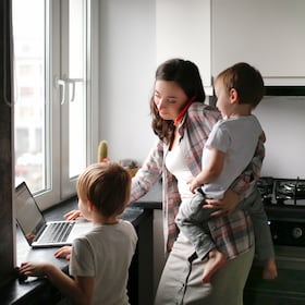 Busy cute woman mom with two children works on a laptop in the kitchen and talks on the phone, mom turns on the kids cartoon. Family concept and freelance work, authentic lifestyle and toning