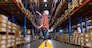 A caucasian female worker pulling a pallet truck in a large distribution center. Woman searching the location of parcel on the shelf for loading the boxes.