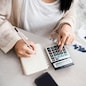 woman writing a list of debt on notebook calculating her expenses with calculator with many invoices , female hand doing accounting