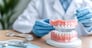 A dentist demonstrates full set of dentures on dental model, showcasing dental tools