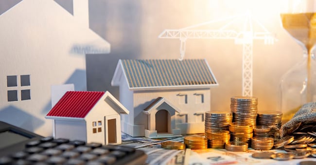 Real estate or property development. Construction business investment concept. Home mortgage loan rate. Coin stack on international banknotes with calculator, house and crane models on the table.