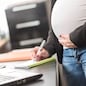 Pregnant woman standing and taking notes at office