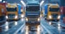 A blue semi truck is driving down a road with two other trucks behind it. The scene is set in a city at night, with the street lights illuminating the area. Scene is one of hustle and bustle