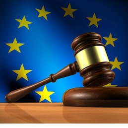 European Union law, legislation and parliament concept with a 3d rendering of a gavel on a wooden desktop and the EU flag on background.