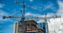 Cranes on modern skyscraper construction in city at sunny day with blue sky