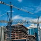 Cranes on modern skyscraper construction in city at sunny day with blue sky