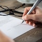 Closeup shot of a woman signing a form. She's writing on a financial contract. Shallow depth of field with focus on tip of the pen.