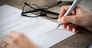 Closeup shot of a woman signing a form. She's writing on a financial contract. Shallow depth of field with focus on tip of the pen.