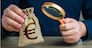 A man examines a euro money bag with a magnifying glass. Checking the origin of capital. Anti money laundering, tax evasion. Study terms and conditions on deposit or loan. Find investments