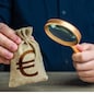 A man examines a euro money bag with a magnifying glass. Checking the origin of capital. Anti money laundering, tax evasion. Study terms and conditions on deposit or loan. Find investments