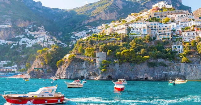 La foto cattura una vista soleggiata di Amalfi da una nave da crociera, mostrando gli edifici colorati della città, le scogliere scoscese e la costa vibrante sotto un cielo blu chiaro in una giornata luminosa. (Shutterstock)