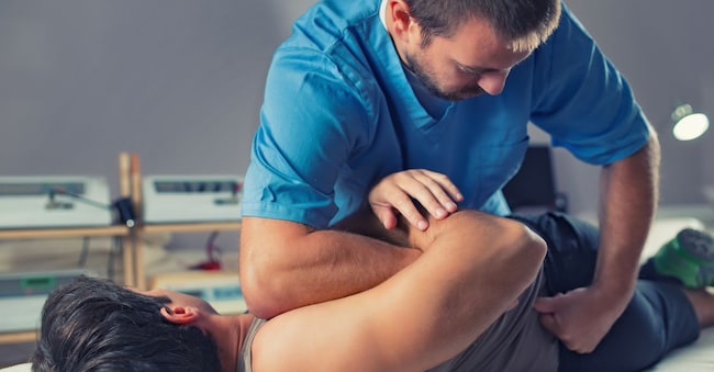 Physiotherapist doing healing treatment on man's back. Therapist wearing blue uniform. Osteopathy. Chiropractic adjustment, patient lying on massage table