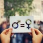 Gender equality concept as woman hands holding a white paper sheet with male and female symbol over a crowded city street background. Sex sign as a metaphor of social issue.