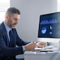 A middle aged businessman focused on his tasks at a well-organized office desk. He is analyzing data on a computer screen while taking notes, showcasing a professional lifestyle, copy space