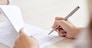 Crop shot of person with pen signing contract at desk in daylight