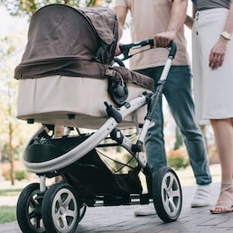 cropped image of mother and father walking with baby carriage in park