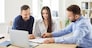 Real estate agent, mortgage broker, bank finance adviser, money loan manager gives pen to young couple clients buyers to sign paper contract after they negotiate his offer at desk with laptop computer