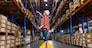 A caucasian female worker pulling a pallet truck in a large distribution center. Woman searching the location of parcel on the shelf for loading the boxes.