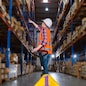 A caucasian female worker pulling a pallet truck in a large distribution center. Woman searching the location of parcel on the shelf for loading the boxes.