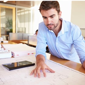 Male Architect With Digital Tablet Studying Plans In Office